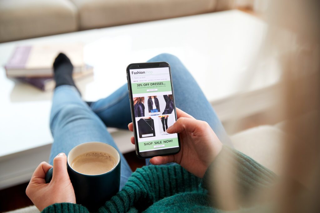 Woman with a cup of tea browsing an online shop on her mobile phone