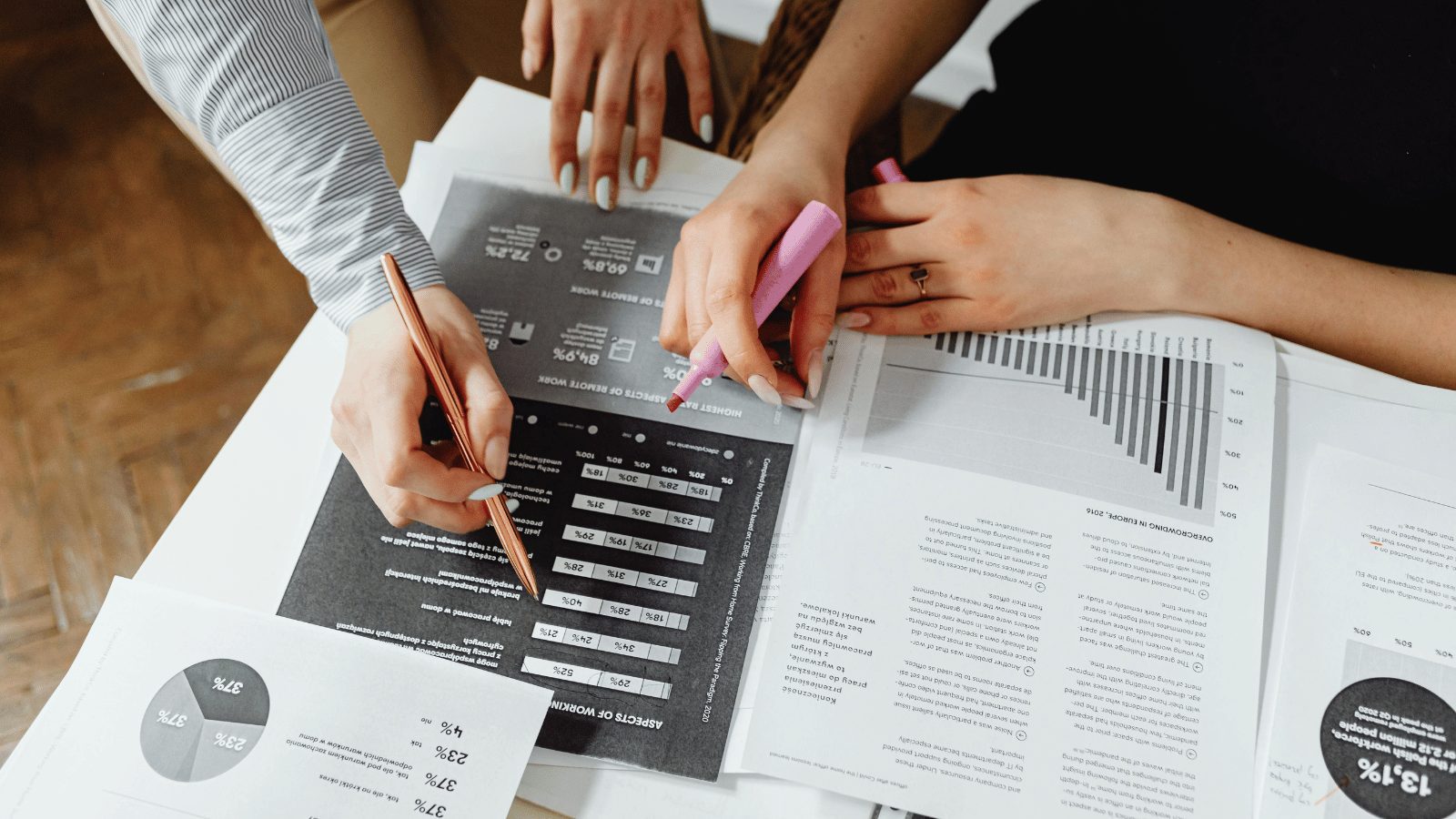Close up of table with lots of printed graphs and tables on it. 2 peoples hands pointing to the tables with pens.