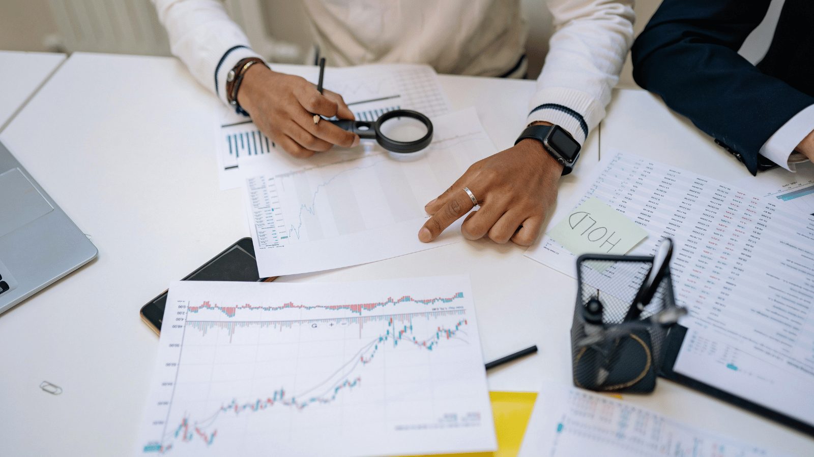 Close up of table with lots of printed graphs and tables on it. Persons hands pointing to the tables.
