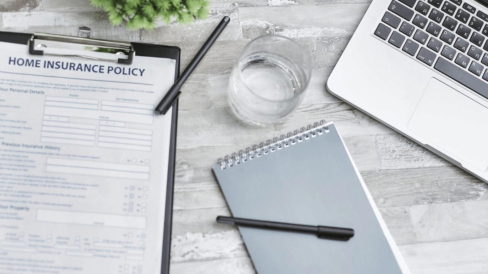 Close up of a table with a clipboard, notepad, laptop and glass of water.