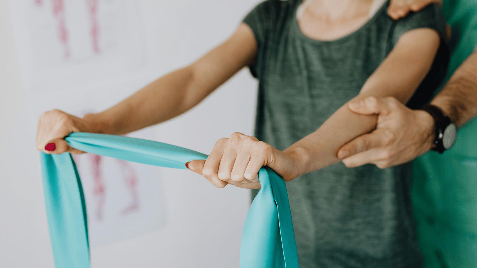 A person in a gray shirt performing a physical therapy or exercise routine using a long, teal-colored resistance band. Another person's hands are visible, assisting with the movement.