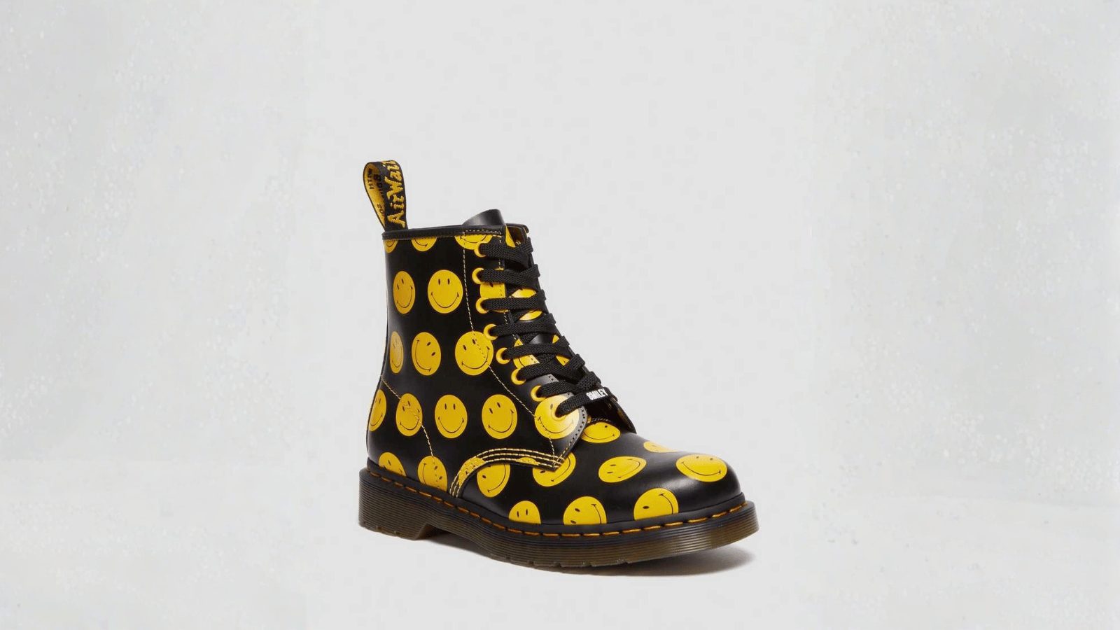 A single black leather lace-up boot, similar to a Dr. Martens style, decorated with an all-over bright yellow 