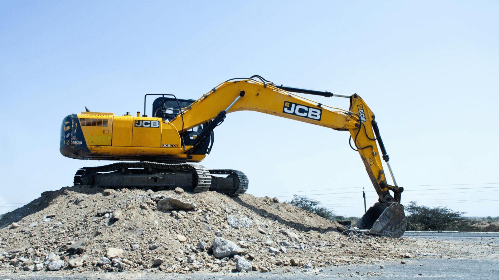A JCB yellow digger ontop of a mound of dirt.