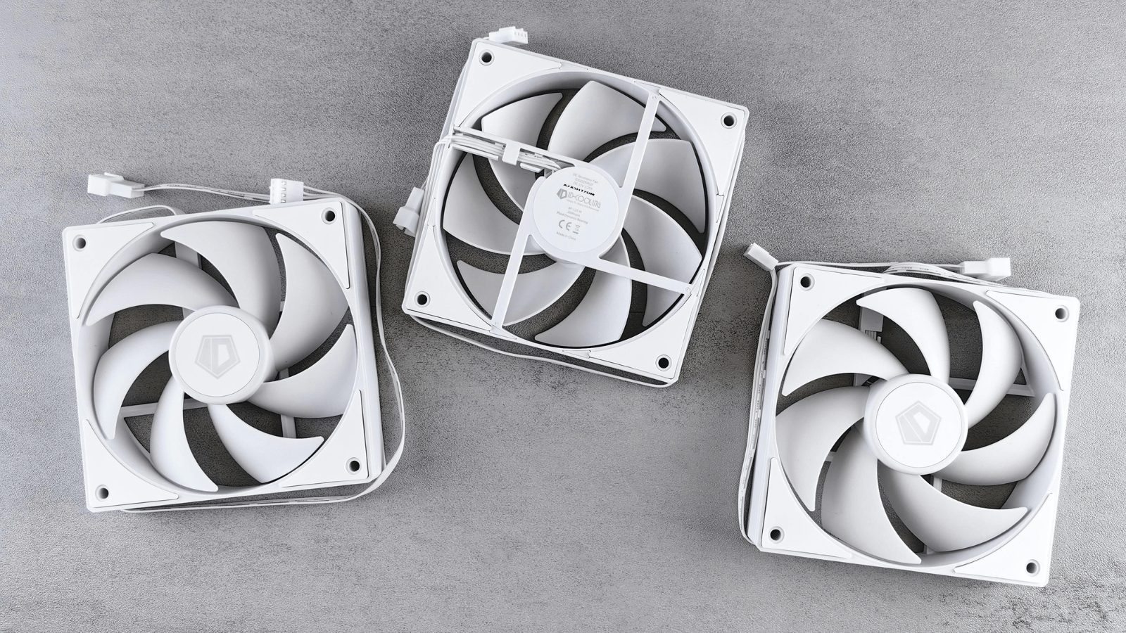 Three white square computer cooling fans laid out on a gray concrete-like surface. Each fan has multiple blades and exposed wiring connectors.